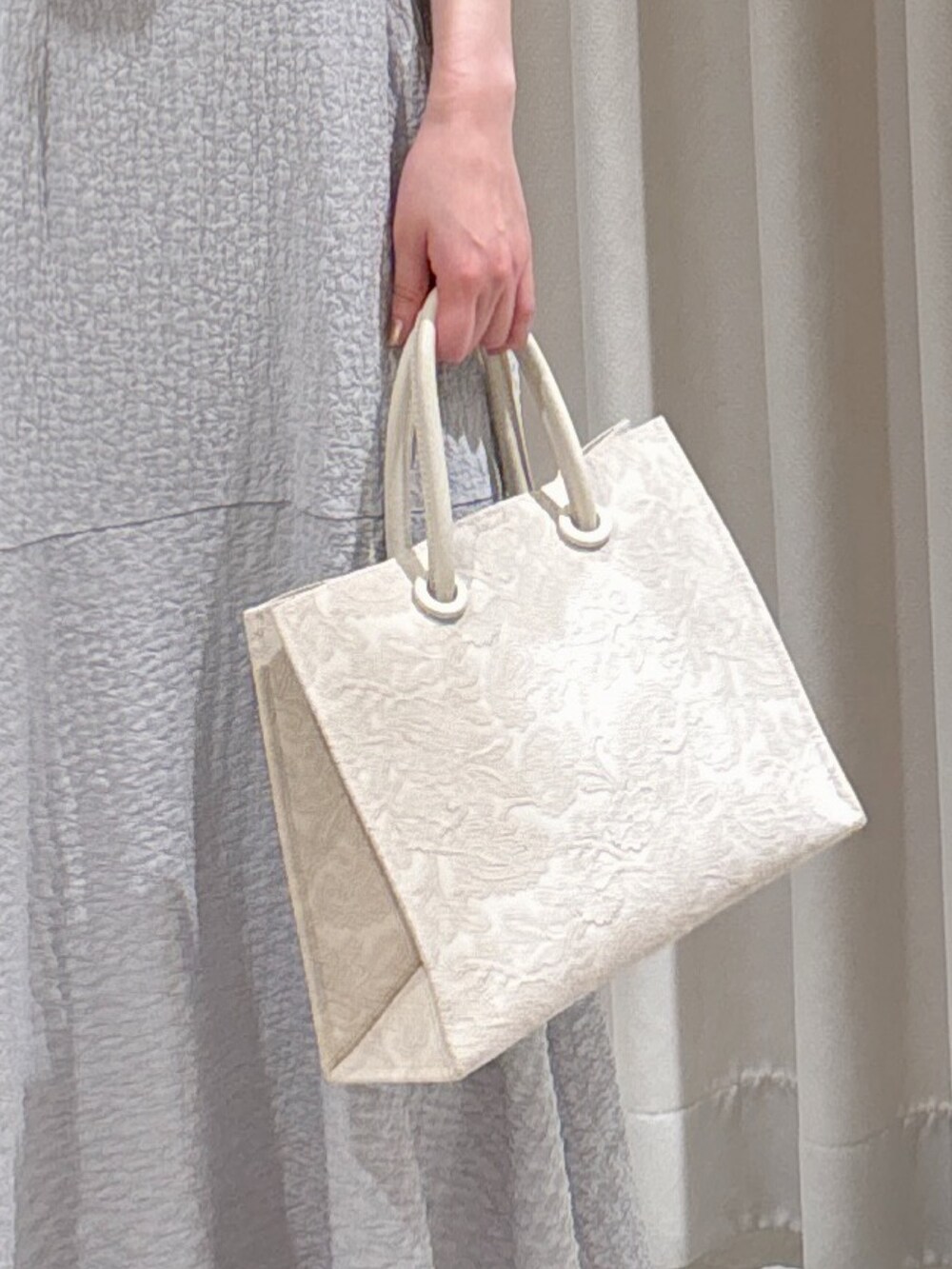 グレー系のワンピース、ホワイト系のトートバッグ、ゴールド系のパンプスを着用したレディースの春コーディネートの4枚目の写真