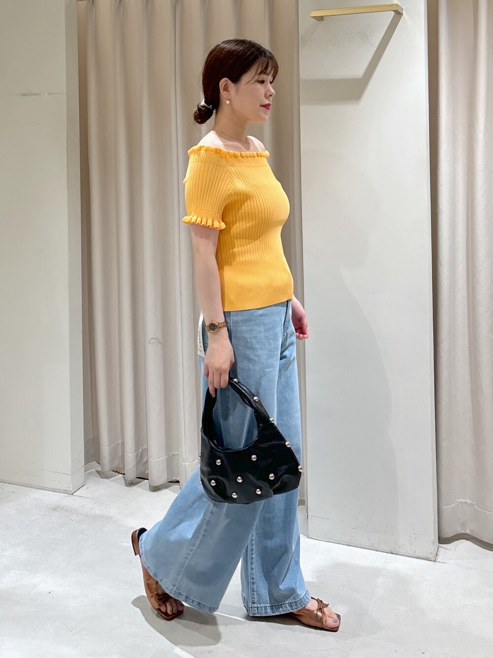 オレンジ系のニット/セーター、ブラック系のハンドバッグ、ブルー系のデニムパンツを着用したレディースの夏コーディネートの2枚目の写真