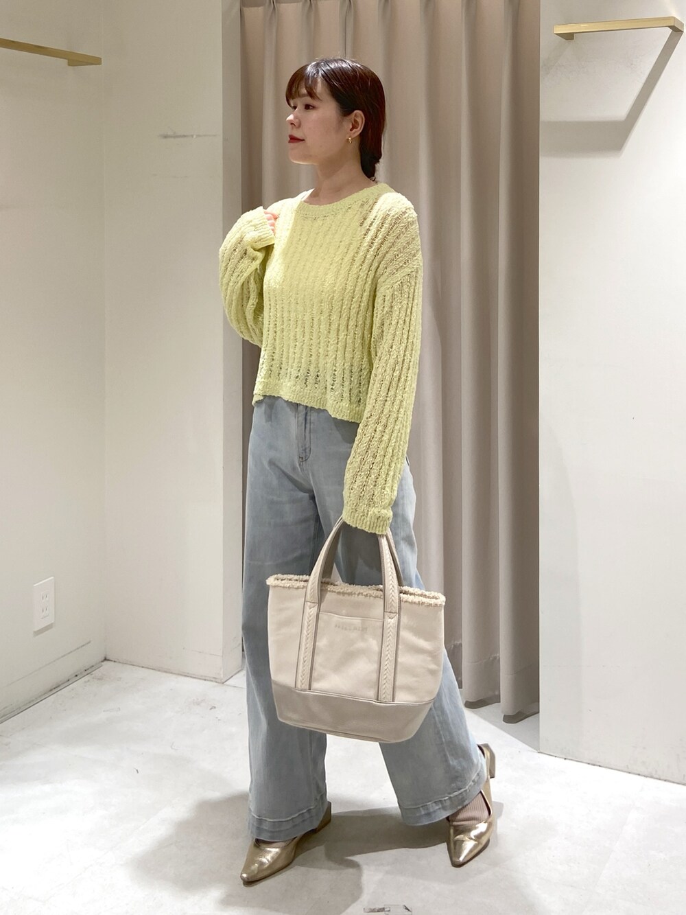 イエロー系のニット/セーター、シルバー系のトートバッグ、ブルー系のデニムパンツを着用したレディースの春コーディネートの3枚目の写真