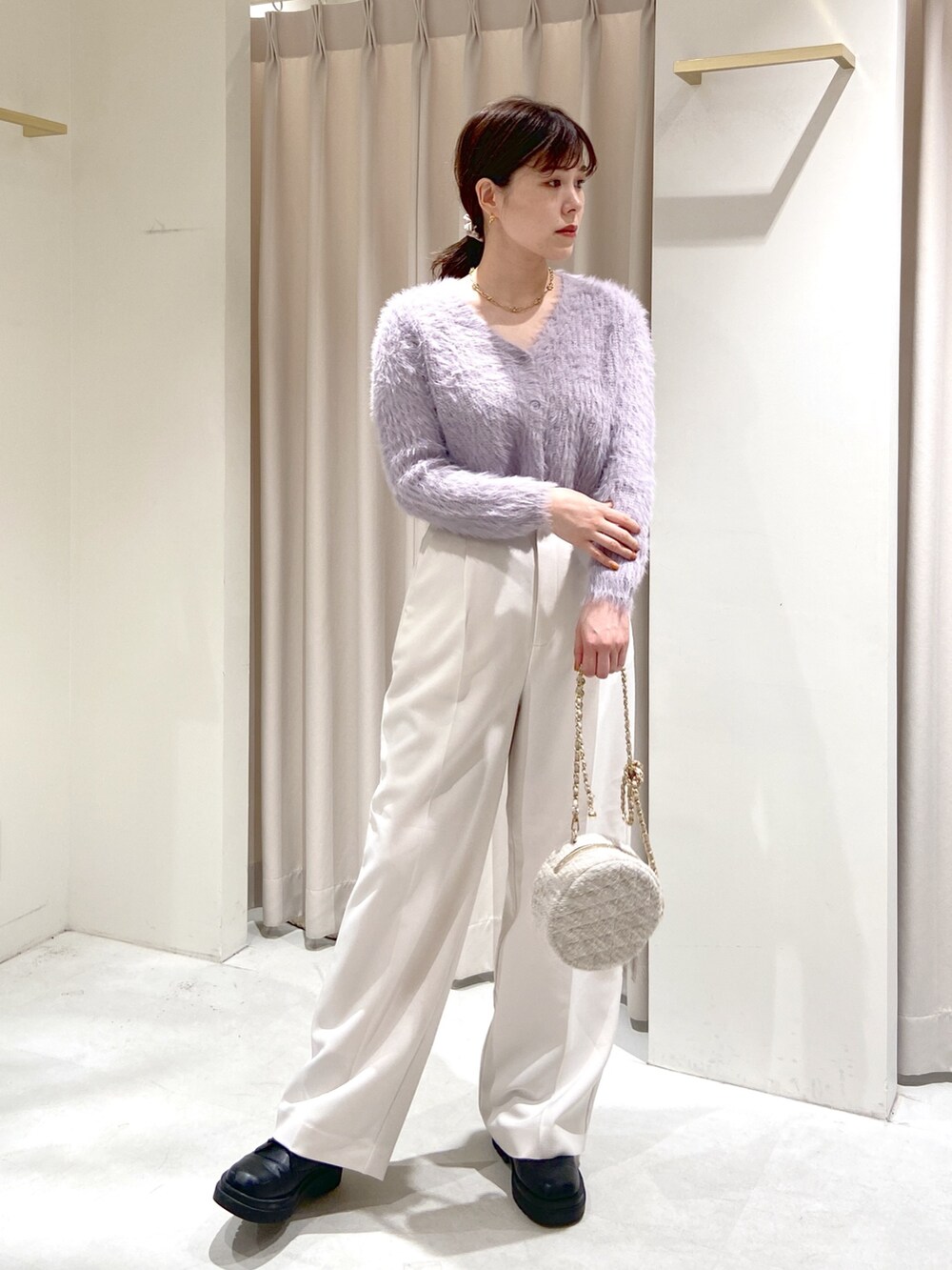 パープル系のカーディガン/ボレロ、ホワイト系のスラックス、ベージュ系のショルダーバッグを着用したレディースの秋コーディネートの2枚目の写真