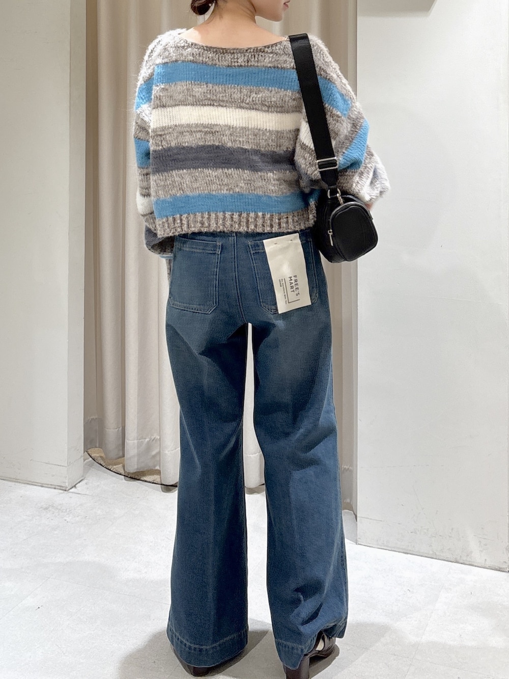 グレー系のニット/セーター、ブラック系のショルダーバッグ、ブルー系のデニムパンツを着用したレディースの秋コーディネートの4枚目の写真