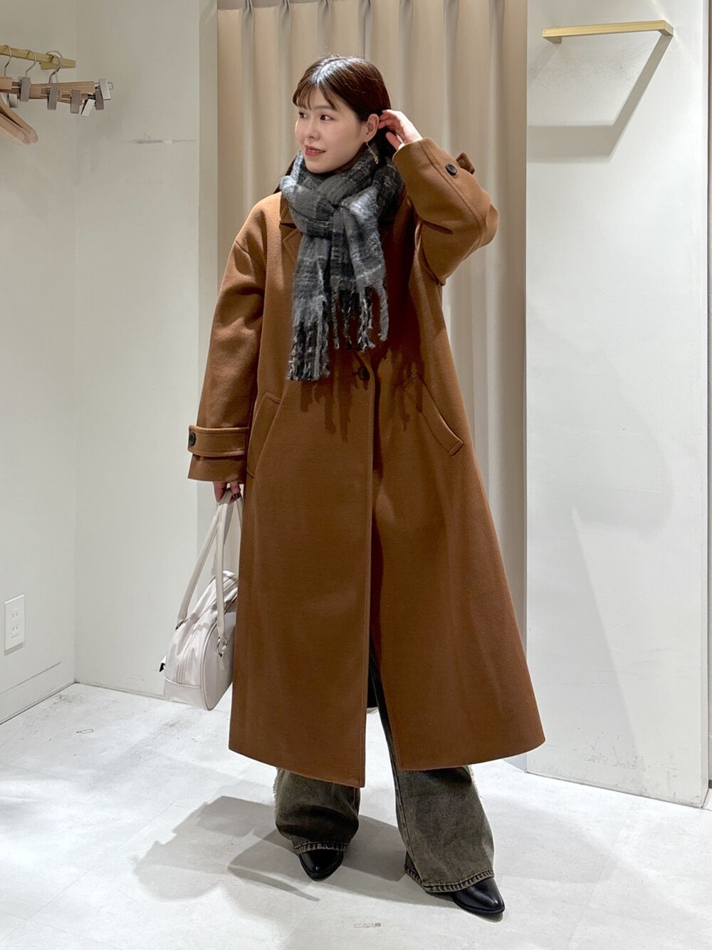 ブラウン系のチェスターコート、ブラック系のニット/セーター、ホワイト系のトートバッグを着用したレディースの秋コーディネートの2枚目の写真