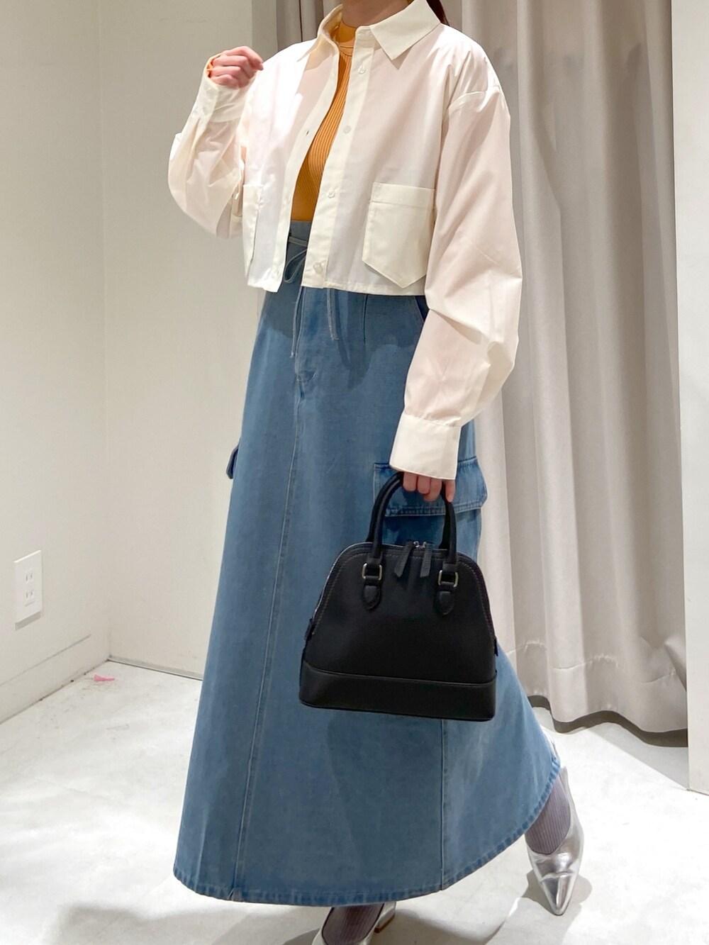 ブルー系のデニムスカート、ホワイト系のシャツ/ブラウス、オレンジ系のニット/セーターを着用したレディースの春コーディネートの3枚目の写真