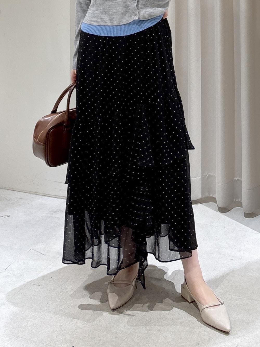 グレー系のニット/セーター、ブラック系のスカート、ブラウン系のハンドバッグを着用したレディースの春コーディネートの3枚目の写真