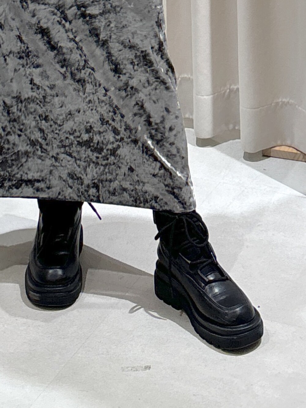 グレー系のステンカラーコート、ホワイト系のショルダーバッグ、ブラック系のブーツを着用したレディースの冬コーディネートの6枚目の写真