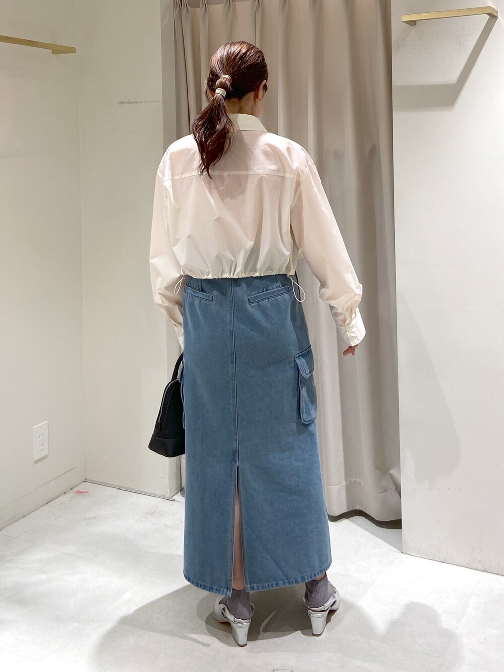 ブルー系のデニムスカート、ホワイト系のシャツ/ブラウス、オレンジ系のニット/セーターを着用したレディースの春コーディネートの2枚目の写真