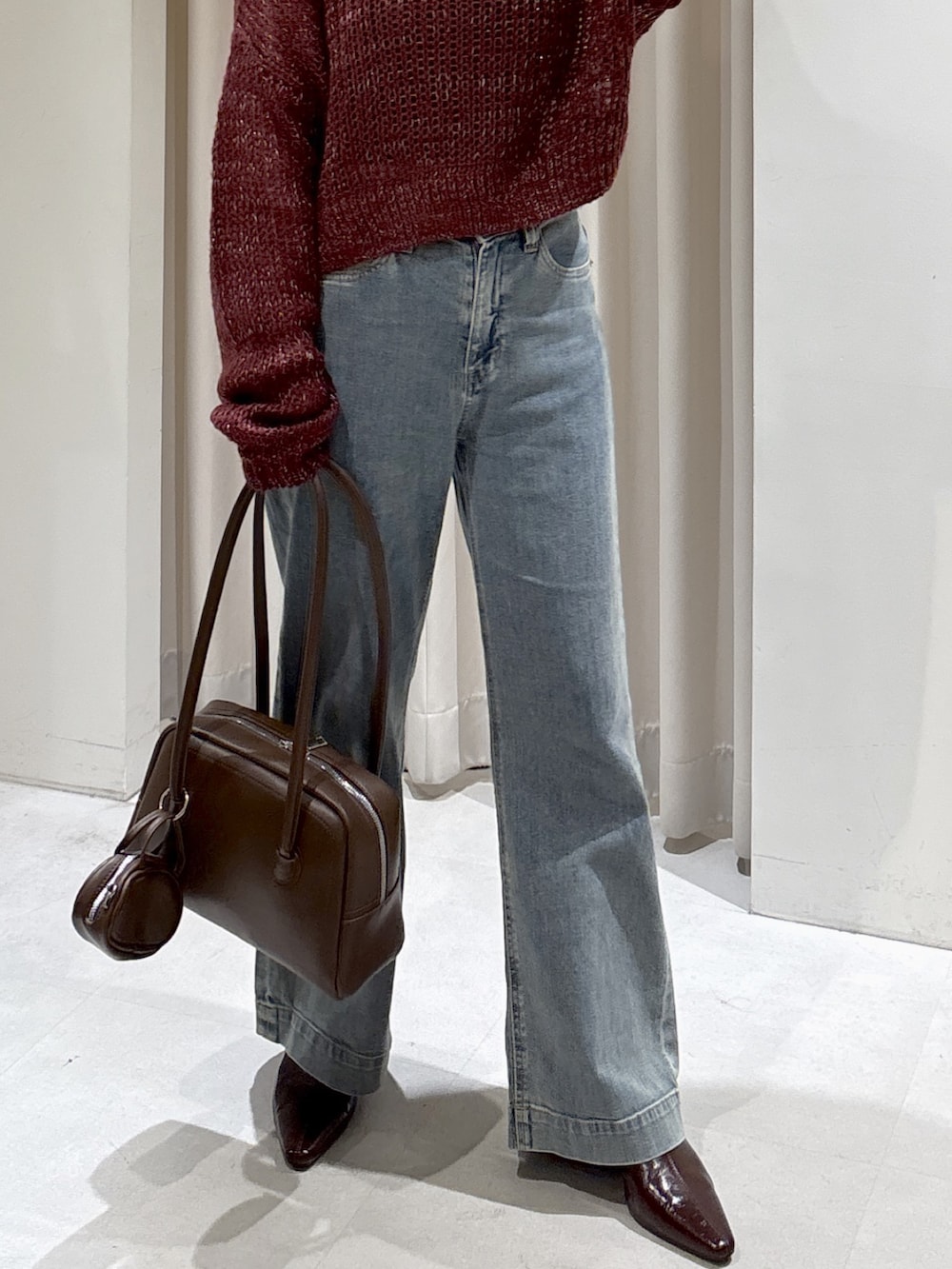 レッド系のニット/セーター、ブラウン系のトートバッグ、ブルー系のデニムパンツを着用したレディースの秋コーディネートの5枚目の写真