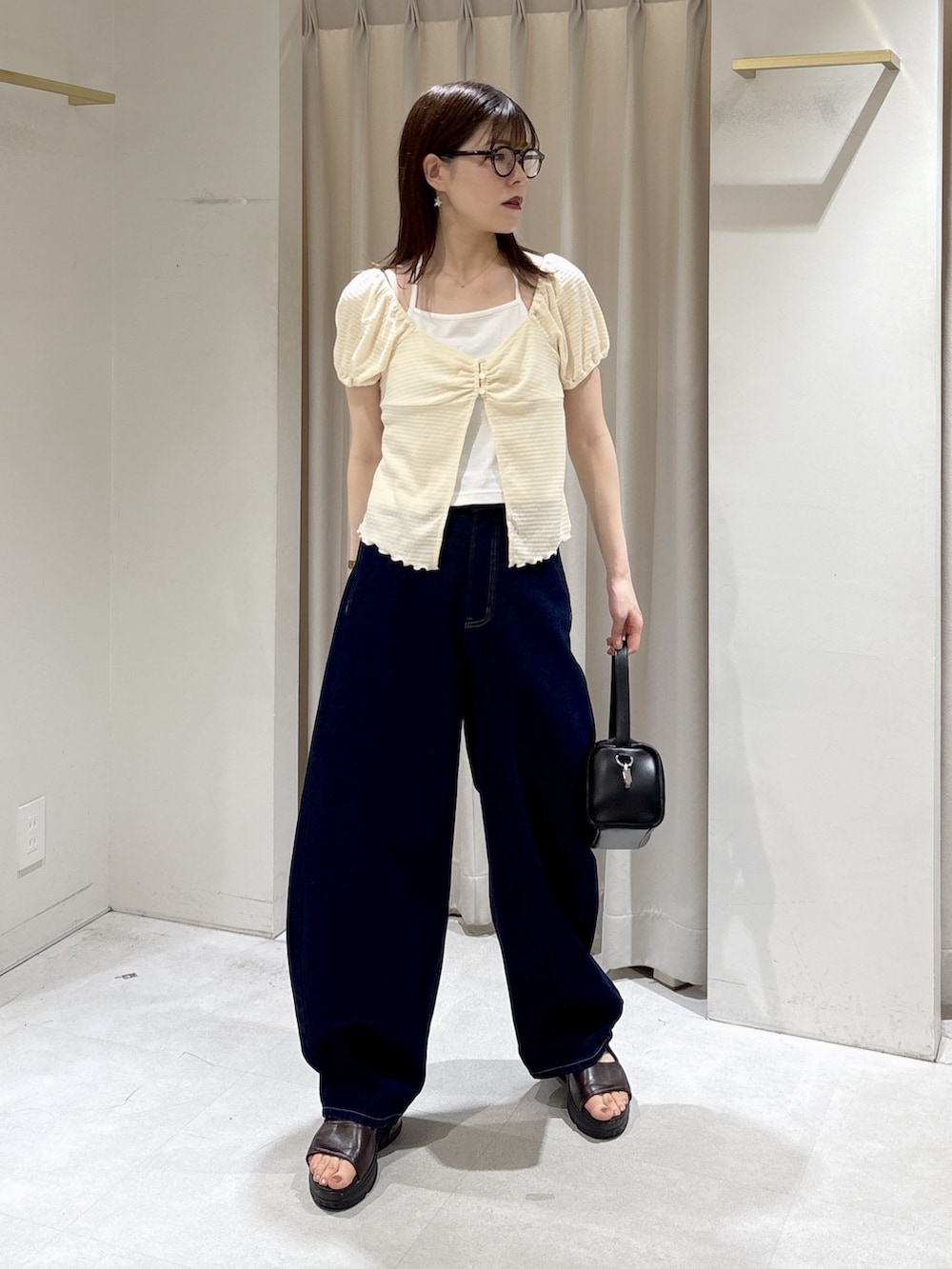 ブルー系のデニムパンツ、ブラック系のハンドバッグ、ブラウン系のサンダルを着用したレディースの夏コーディネートの2枚目の写真