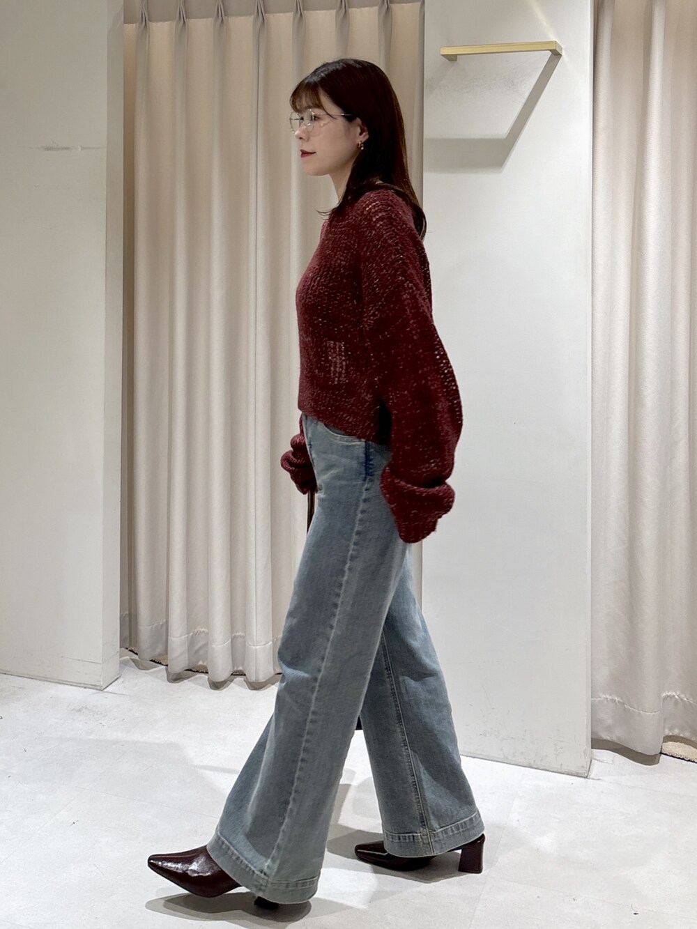 レッド系のニット/セーター、ブラウン系のトートバッグ、ブルー系のデニムパンツを着用したレディースの秋コーディネートの4枚目の写真