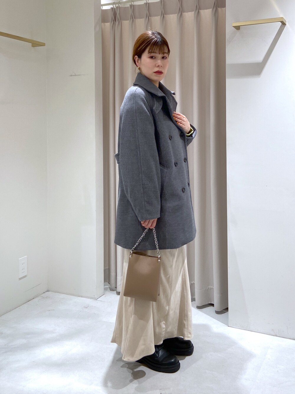 グレー系のステンカラーコート、グリーン系のニット/セーター、ベージュ系のショルダーバッグを着用したレディースの秋コーディネートの2枚目の写真