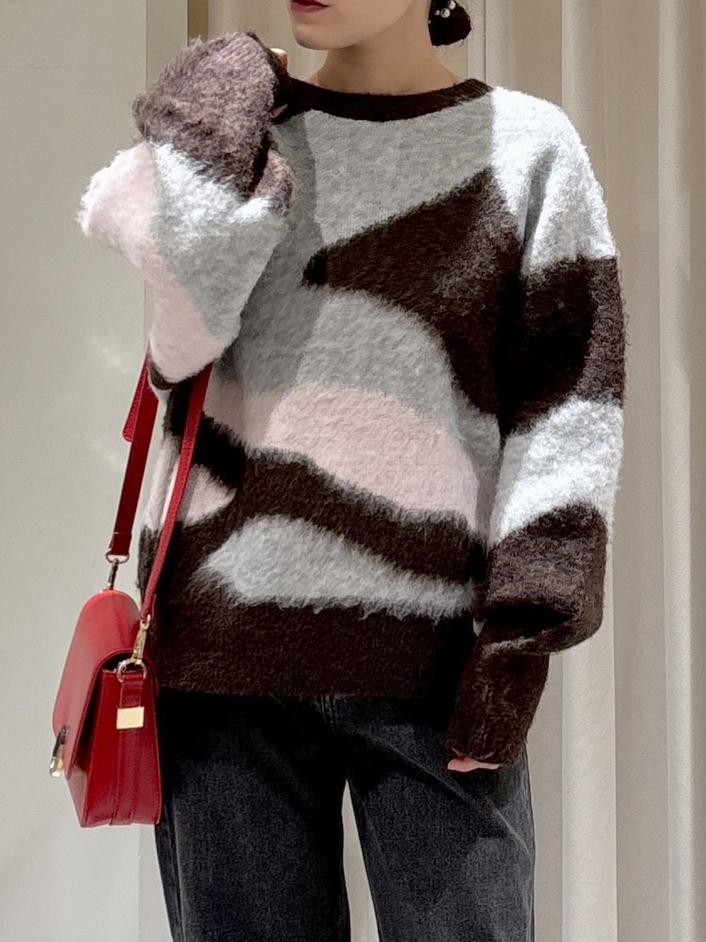 ブラウン系のニット/セーター、レッド系のハンドバッグ、ブラック系のデニムパンツを着用したレディースの秋コーディネートの2枚目の写真