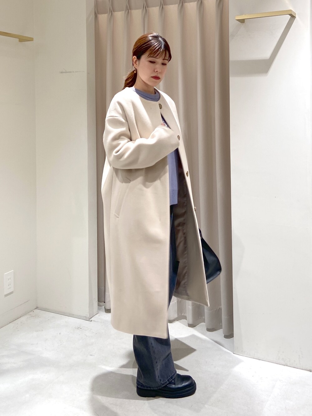 ベージュ系のノーカラーコート、ブルー系のニット/セーター、ブラック系のショルダーバッグを着用したレディースの冬コーディネートの3枚目の写真