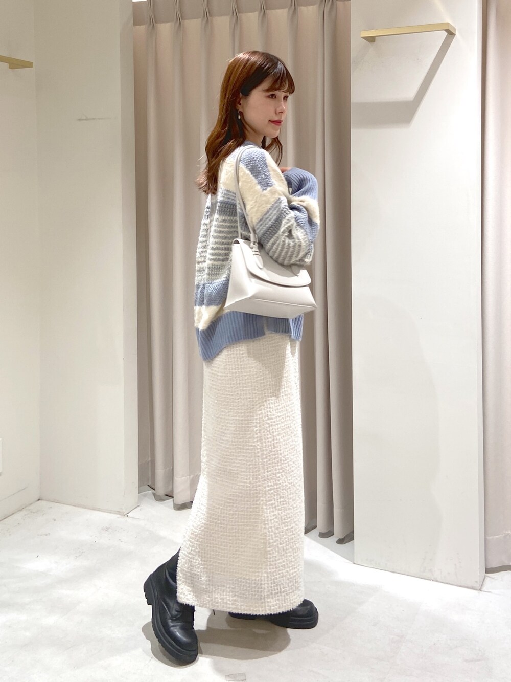 ブルー系のニット/セーター、ホワイト系のスカート、ブラック系のブーツを着用したレディースの冬コーディネートの2枚目の写真