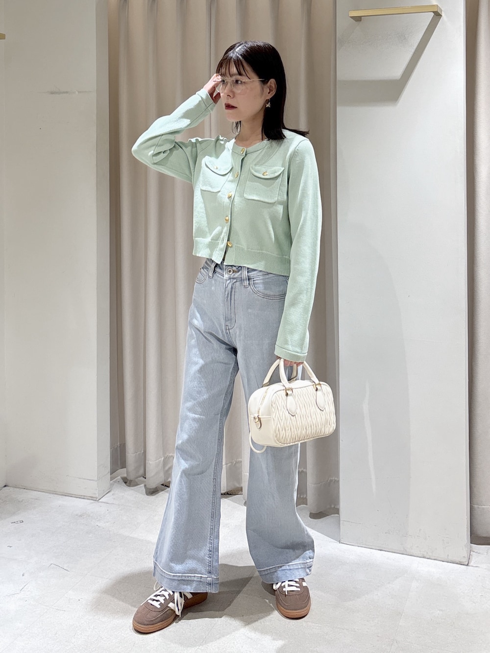 グリーン系のニット/セーター、ホワイト系のボストンバッグ、ブルー系のデニムパンツを着用したレディースの春コーディネートの4枚目の写真