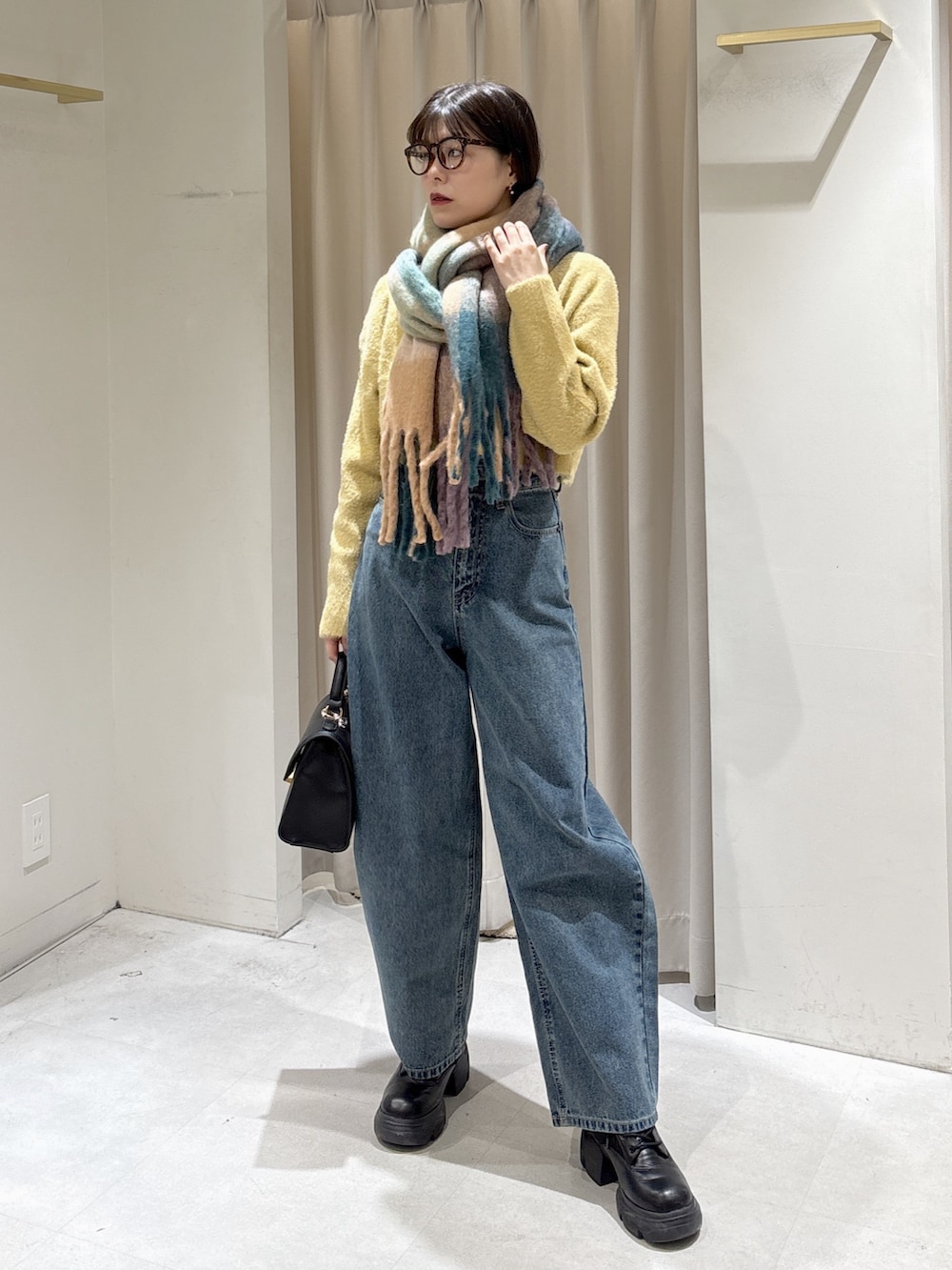 イエロー系のニット/セーター、ブラック系のトートバッグ、ブルー系のデニムパンツを着用したレディースの冬コーディネートの2枚目の写真
