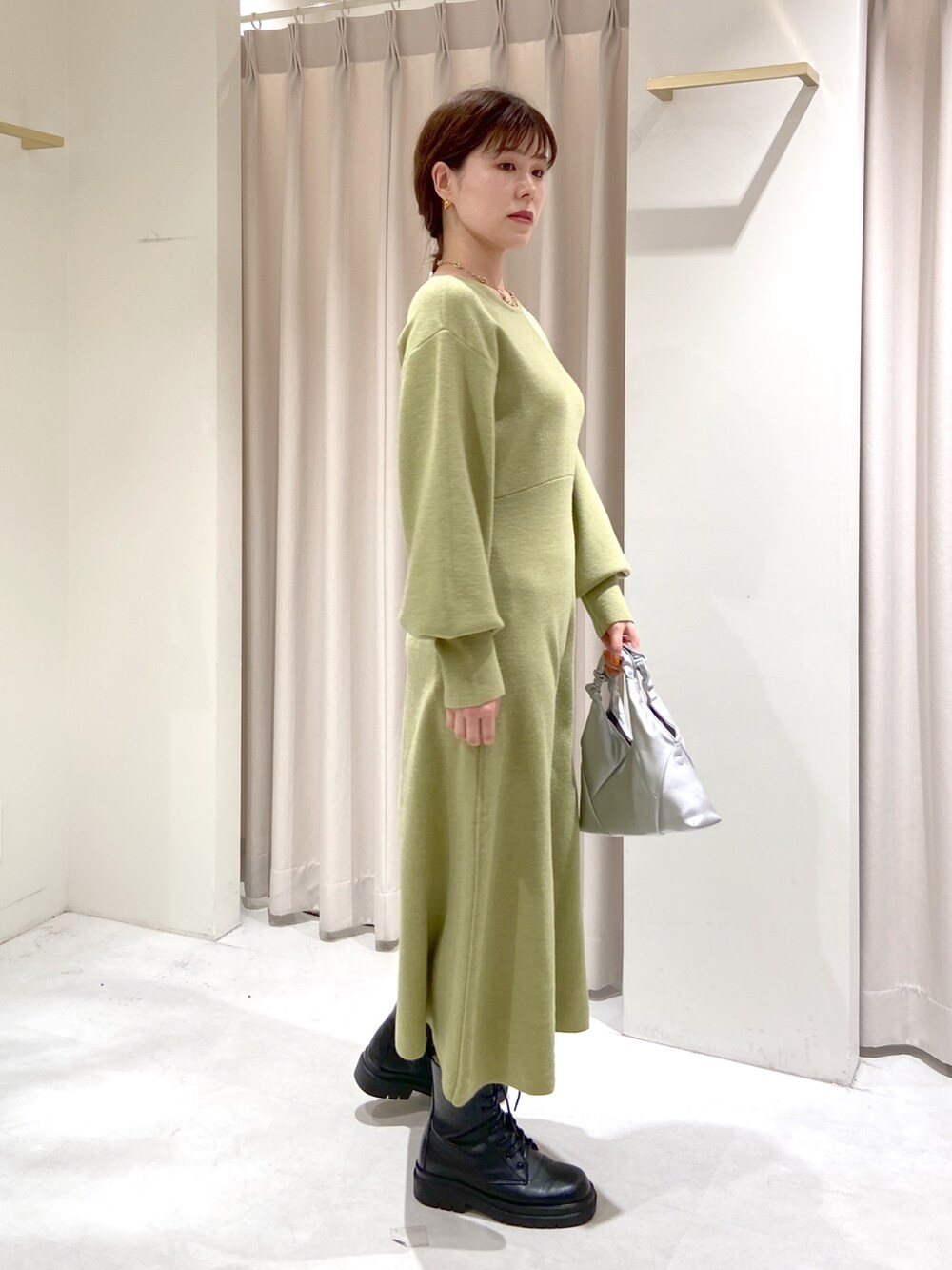 シルバー系のショルダーバッグ、ブラック系のブーツ、グリーン系のワンピースを着用したレディースの冬コーディネートの3枚目の写真