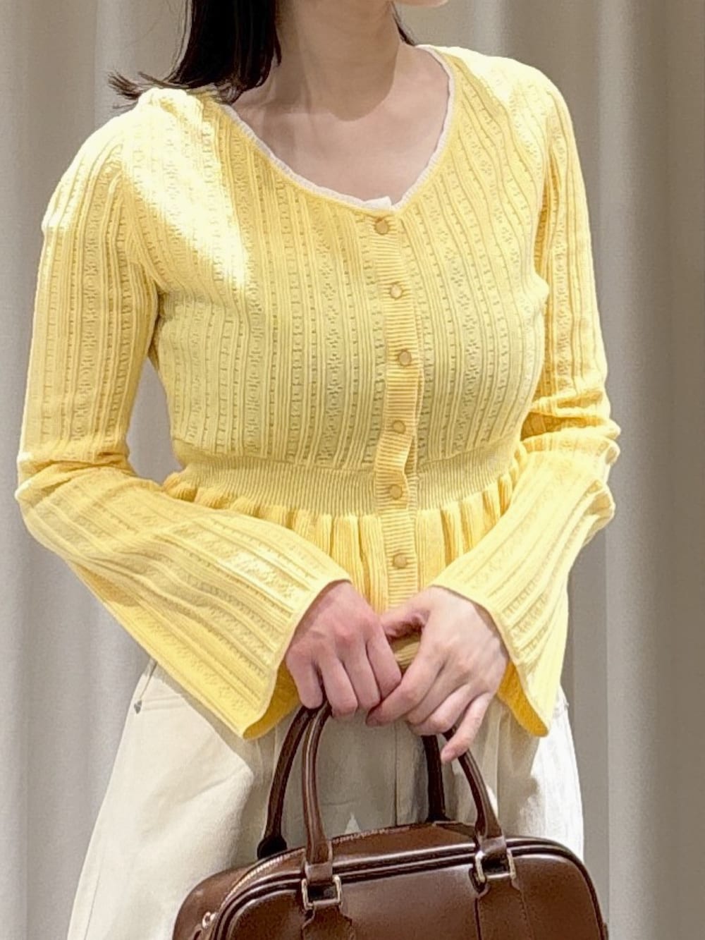 イエロー系のニット/セーター、ホワイト系のその他パンツ、ブラウン系のハンドバッグを着用したレディースの春コーディネートの2枚目の写真