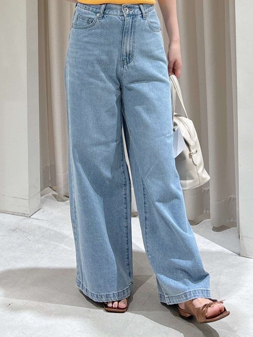 オレンジ系のニット/セーター、ブラック系のハンドバッグ、ブルー系のデニムパンツを着用したレディースの夏コーディネートの5枚目の写真