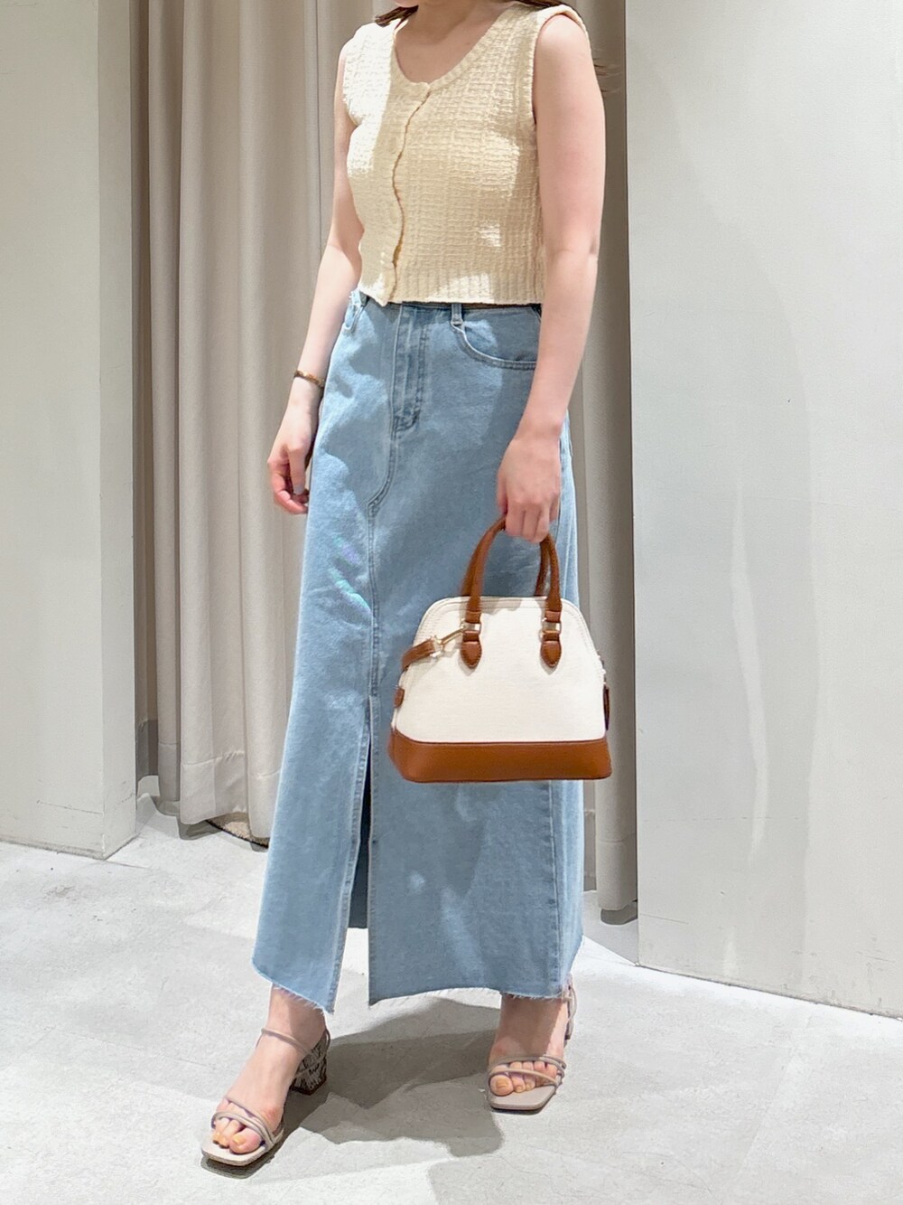 ホワイト系のベスト、ブルー系のデニムスカート、グレー系のサンダルを着用したレディースの春コーディネートの2枚目の写真