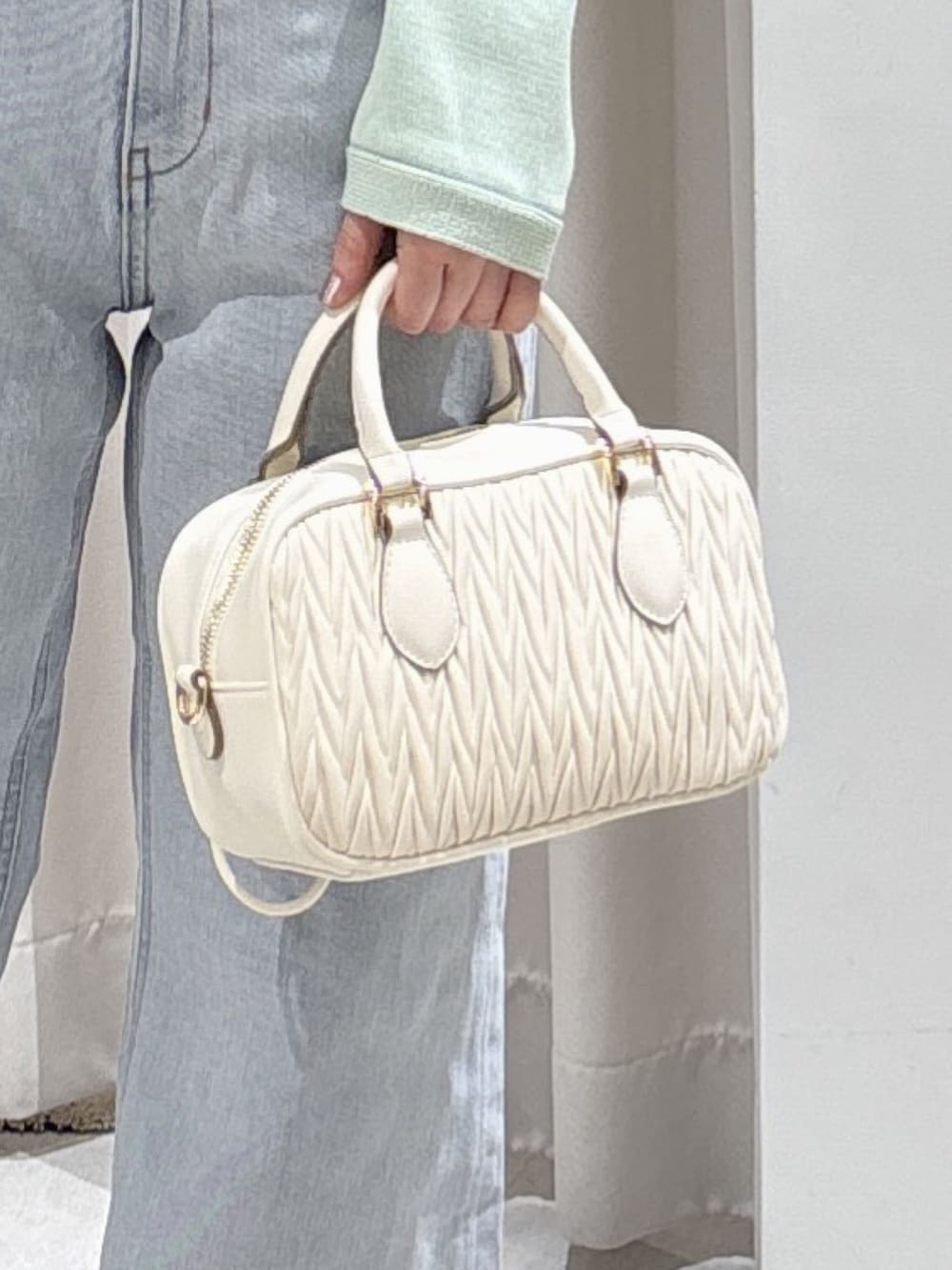 グリーン系のニット/セーター、ホワイト系のボストンバッグ、ブルー系のデニムパンツを着用したレディースの春コーディネートの5枚目の写真