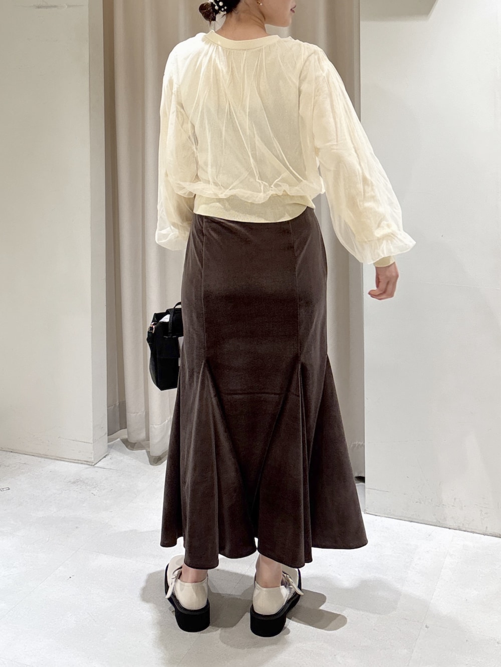 イエロー系のニット/セーター、ブラウン系のスカート、ブラック系のショルダーバッグを着用したレディースの冬コーディネートの2枚目の写真