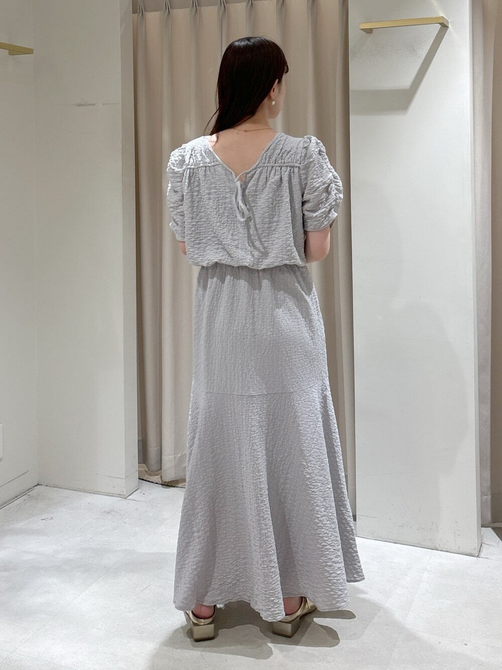 グレー系のワンピース、ホワイト系のトートバッグ、ゴールド系のパンプスを着用したレディースの春コーディネートの3枚目の写真