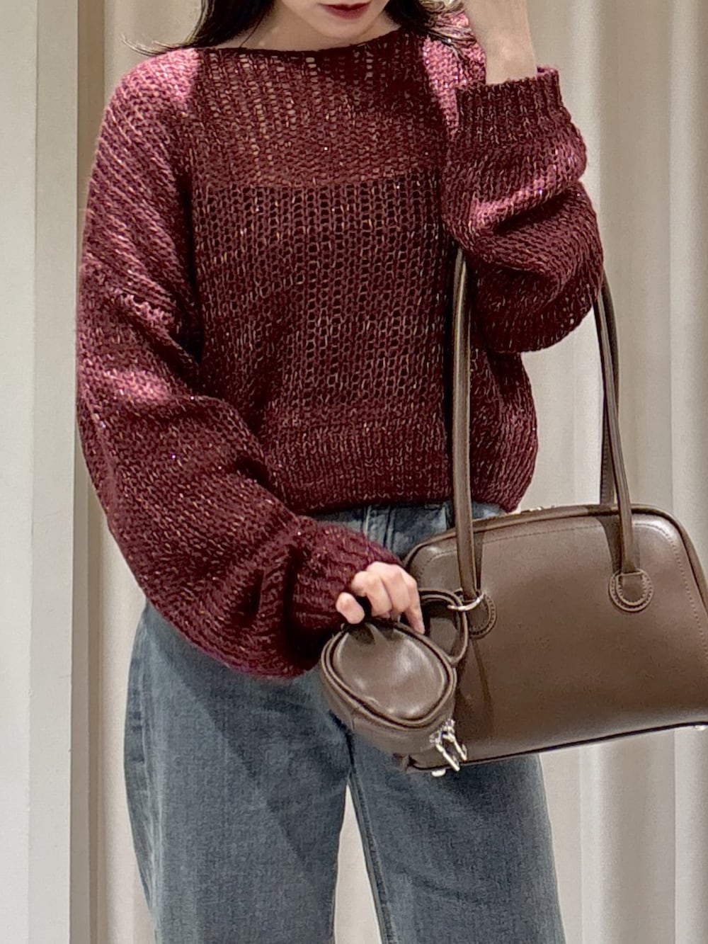 レッド系のニット/セーター、ブラウン系のトートバッグ、ブルー系のデニムパンツを着用したレディースの秋コーディネートの6枚目の写真