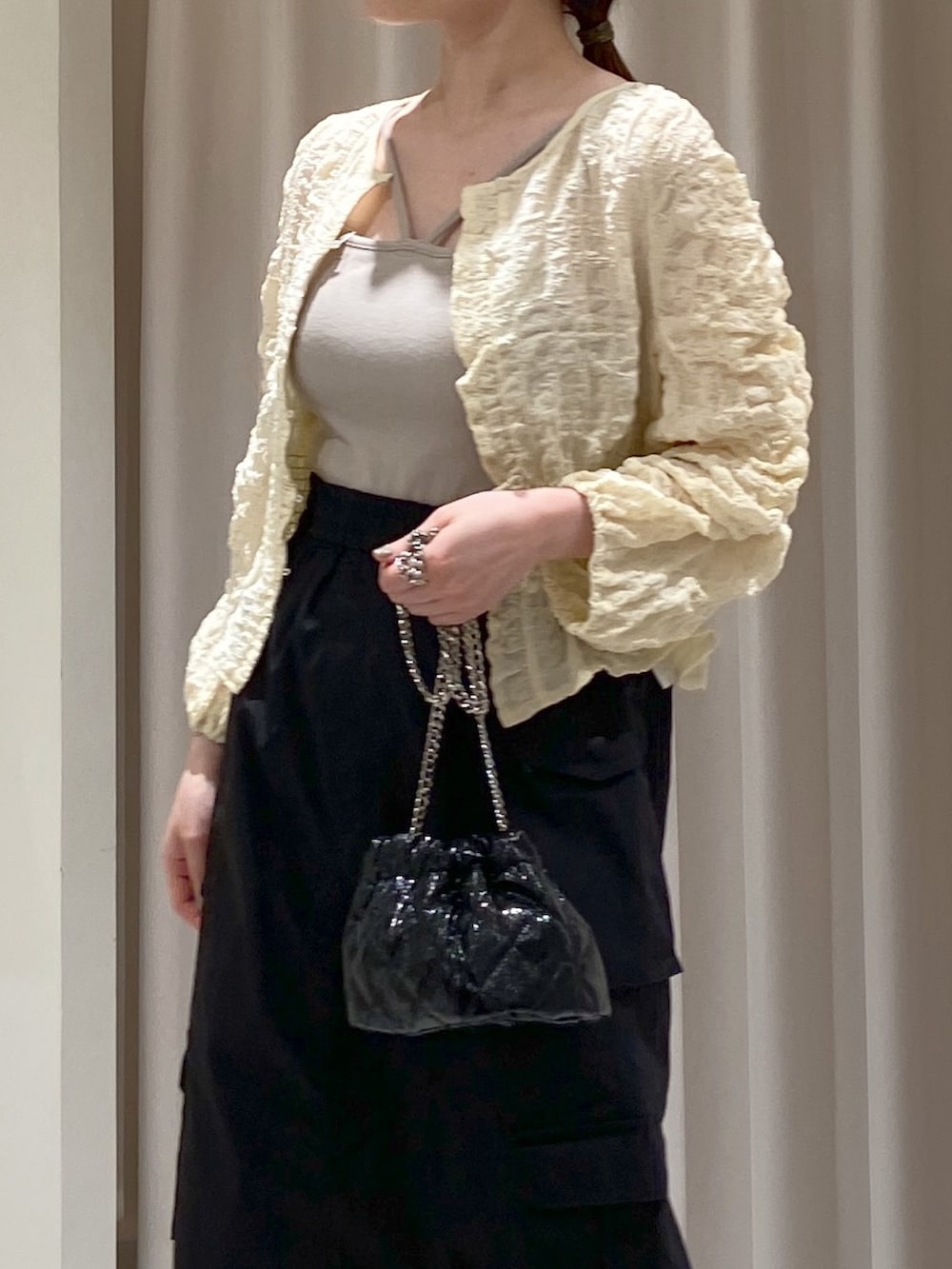 ホワイト系のカーディガン/ボレロ、グレー系のキャミソール、ブラック系のショルダーバッグを着用したレディースの春コーディネートの2枚目の写真