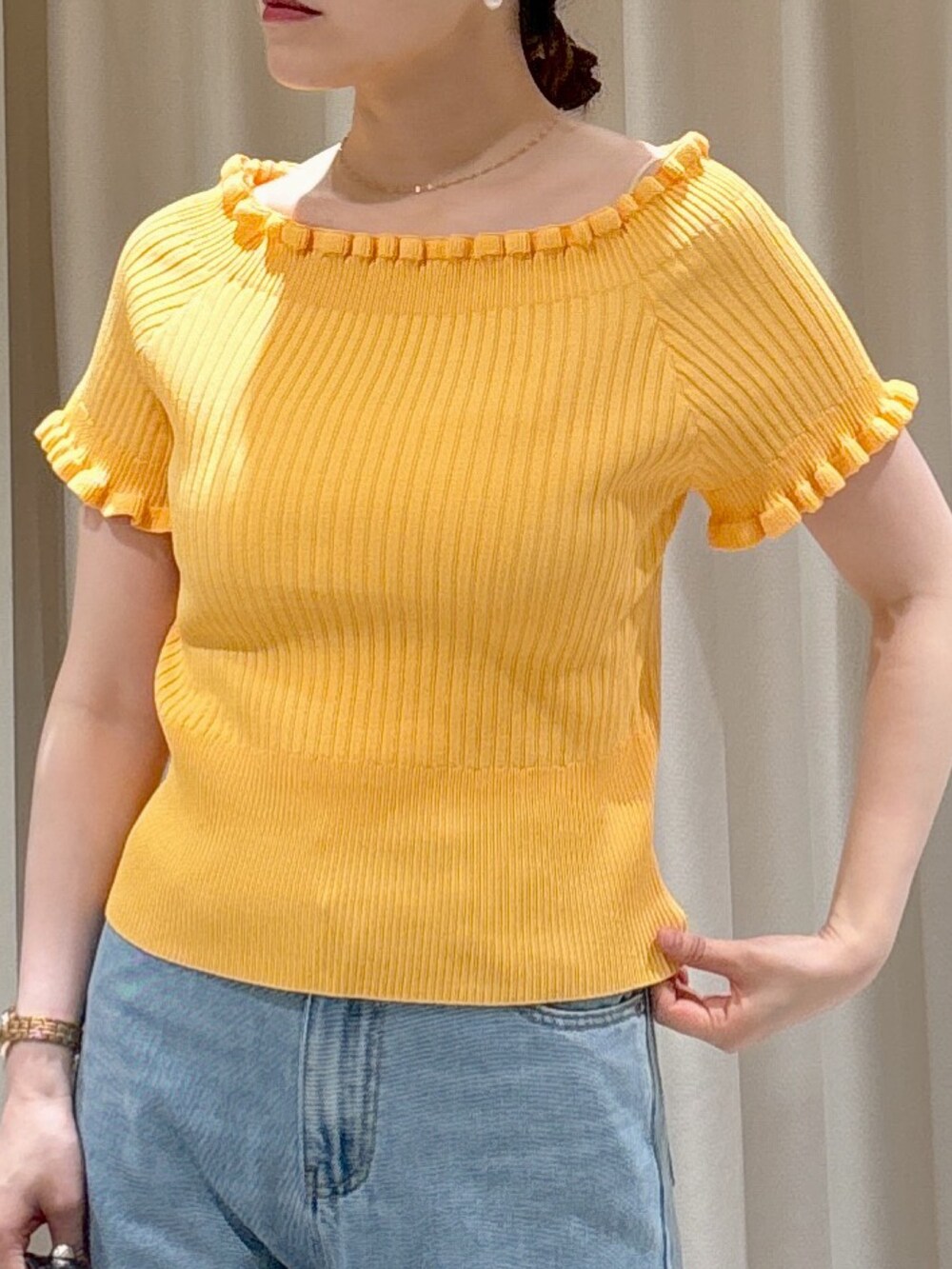 オレンジ系のニット/セーター、ブラック系のハンドバッグ、ブルー系のデニムパンツを着用したレディースの夏コーディネートの4枚目の写真