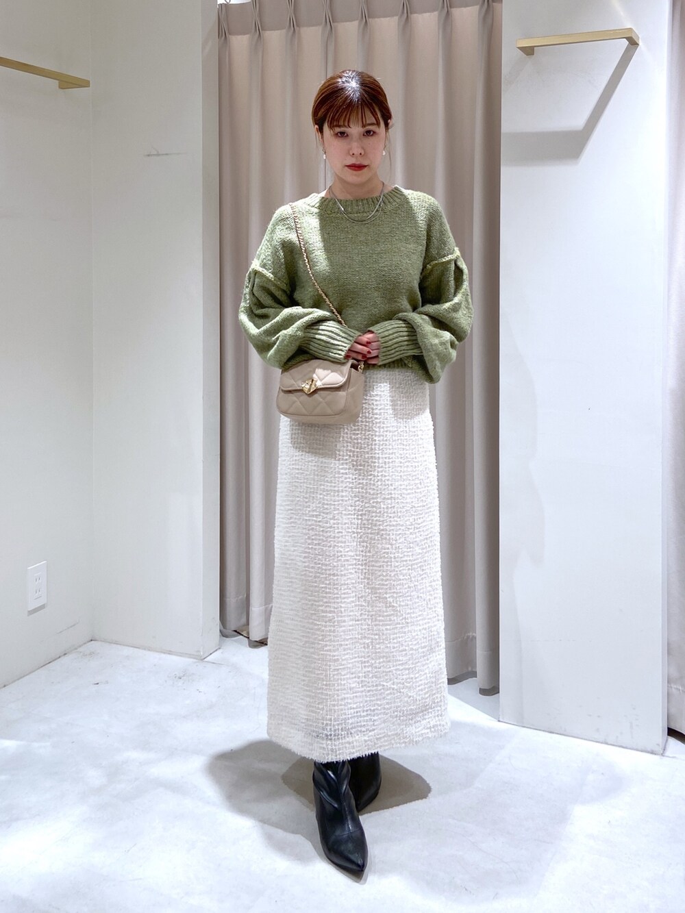 グリーン系のニット/セーター、ホワイト系のスカート、ベージュ系のショルダーバッグを着用したレディースの秋コーディネートの2枚目の写真