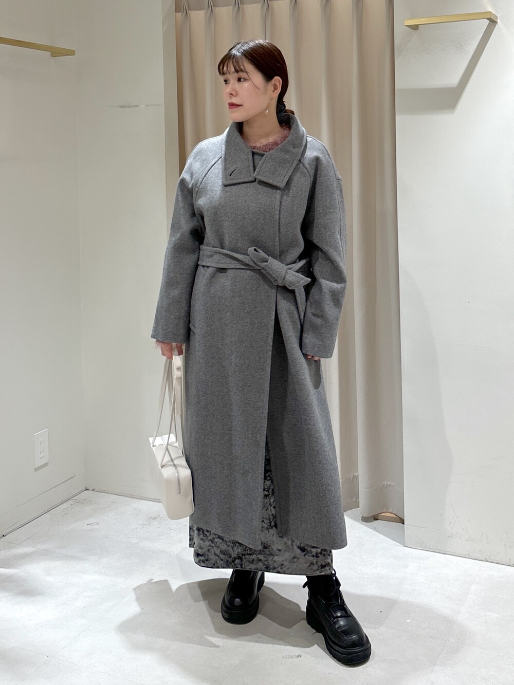 グレー系のステンカラーコート、ホワイト系のショルダーバッグ、ブラック系のブーツを着用したレディースの冬コーディネートの8枚目の写真