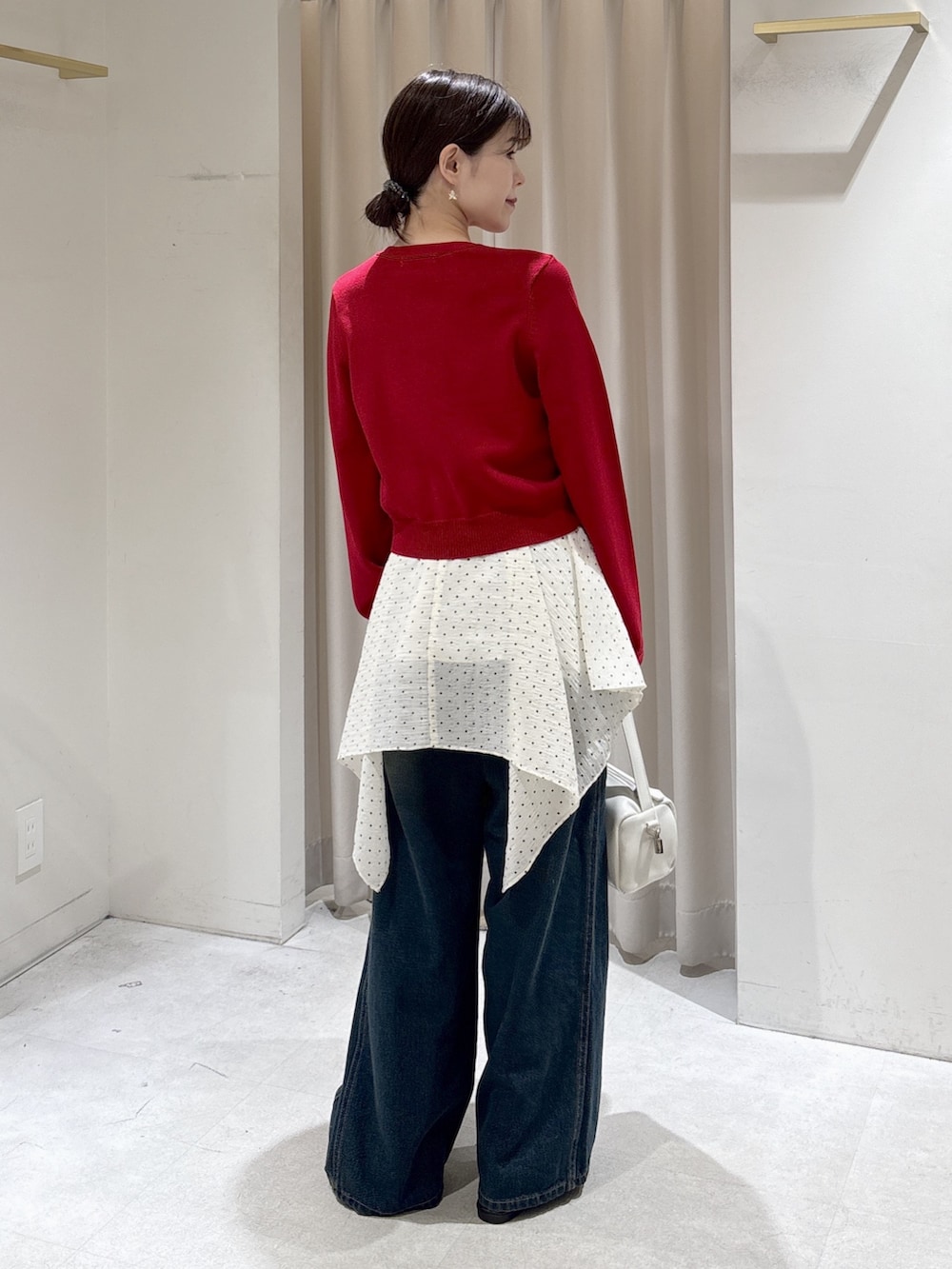 レッド系のニット/セーター、ホワイト系のワンピース、ブルー系のデニムパンツを着用したレディースの春コーディネートの3枚目の写真