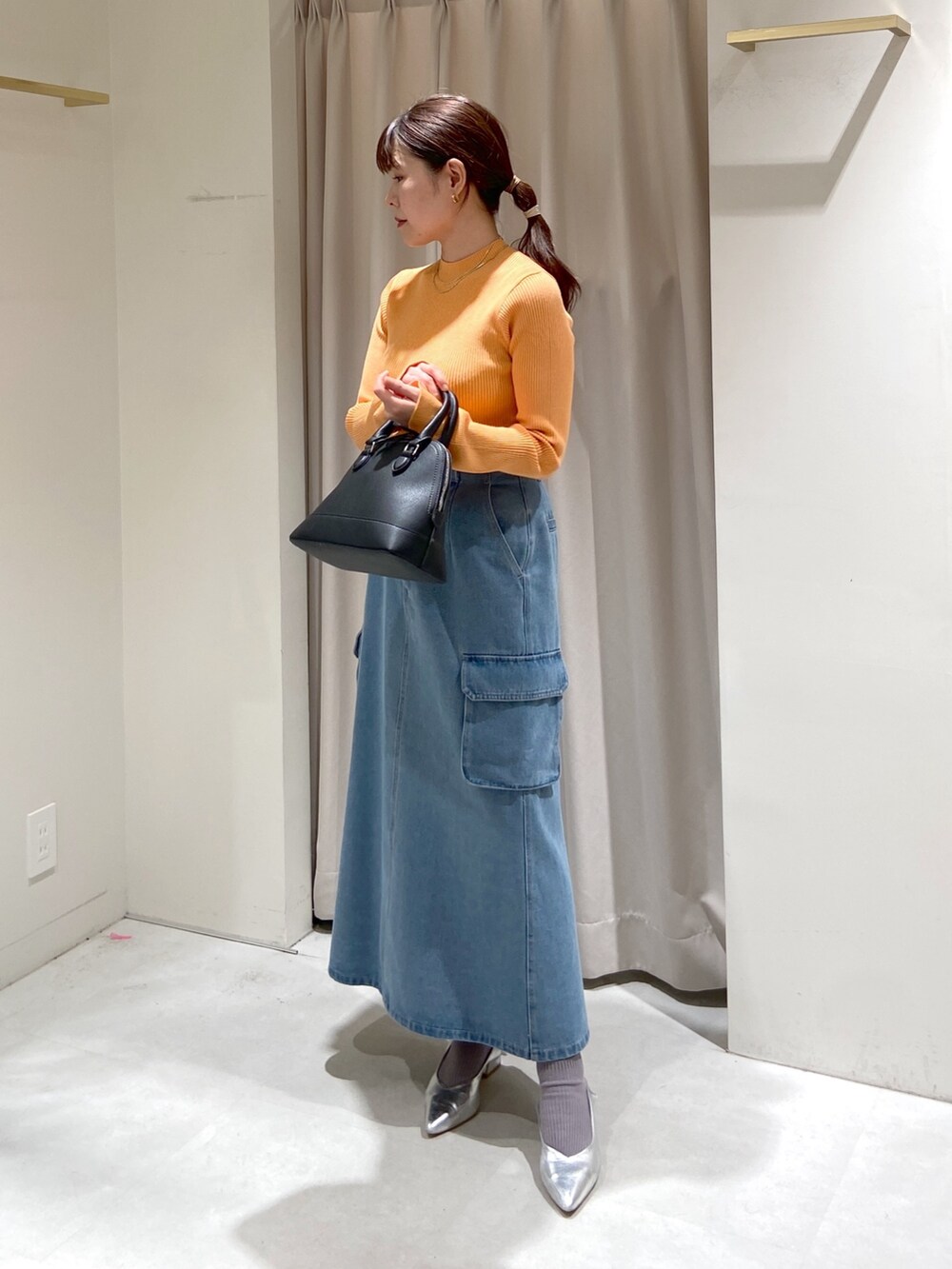 ブルー系のデニムスカート、ホワイト系のシャツ/ブラウス、オレンジ系のニット/セーターを着用したレディースの春コーディネートの6枚目の写真