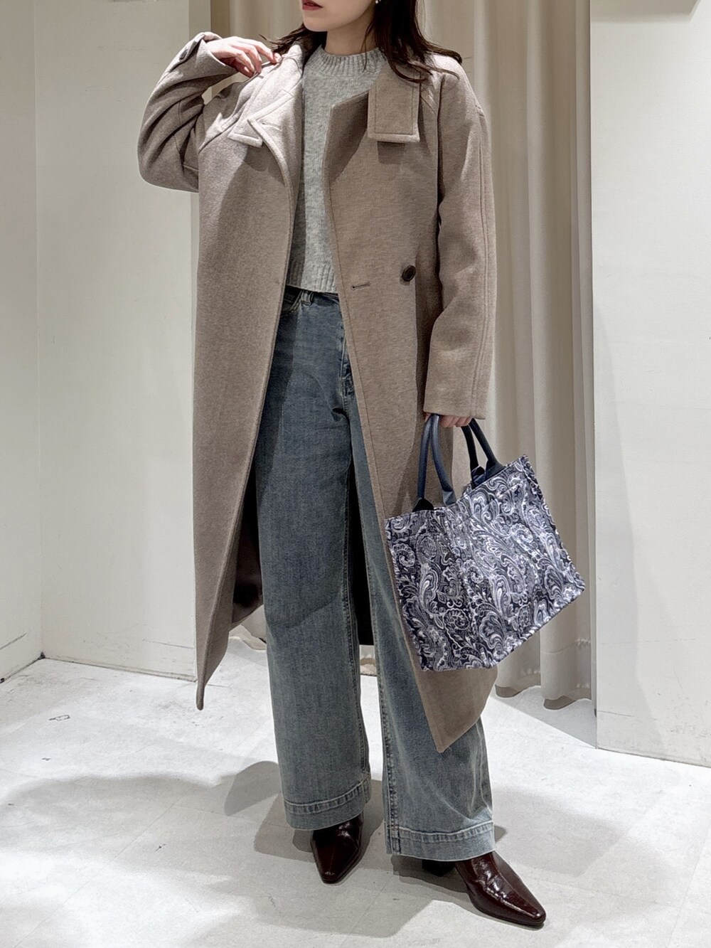 ブラウン系のステンカラーコート、ブルー系のトートバッグ、ブルー系のデニムパンツを着用したレディースの秋コーディネートの3枚目の写真