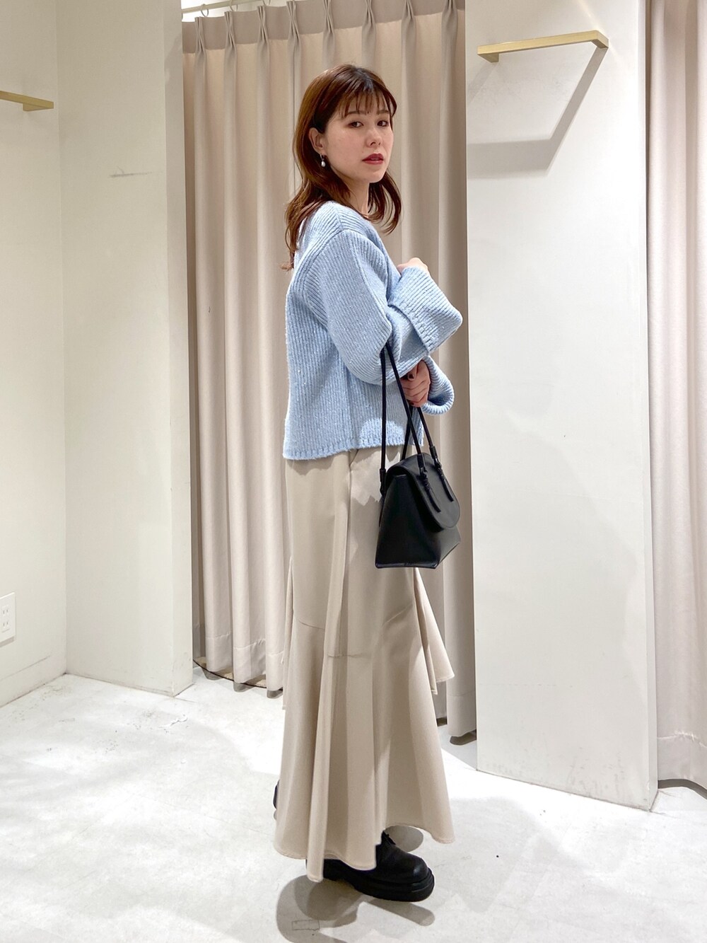 ブルー系のニット/セーター、ベージュ系のスカート、ブラック系のショルダーバッグを着用したレディースの冬コーディネートの2枚目の写真