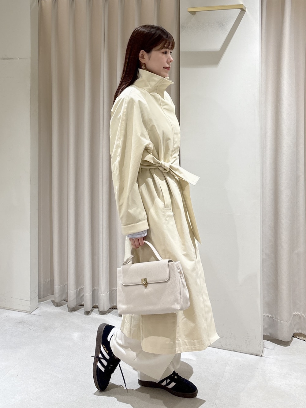 ホワイト系のトレンチコート、ベージュ系のニット/セーター、ブラック系のスニーカーを着用したレディースの冬コーディネートの2枚目の写真