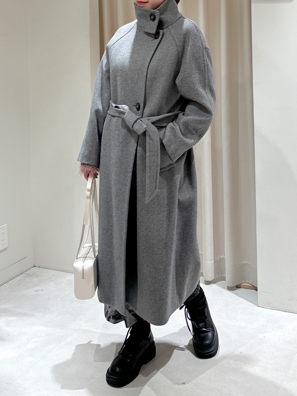 グレー系のステンカラーコート、ホワイト系のショルダーバッグ、ブラック系のブーツを着用したレディースの冬コーディネートの2枚目の写真