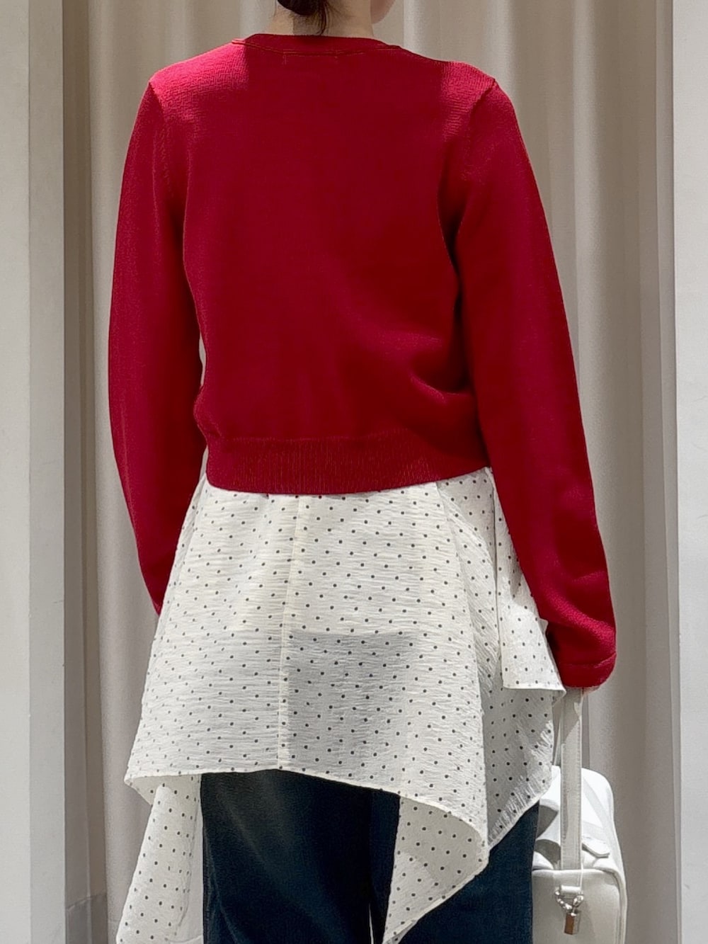 レッド系のニット/セーター、ホワイト系のワンピース、ブルー系のデニムパンツを着用したレディースの春コーディネートの5枚目の写真