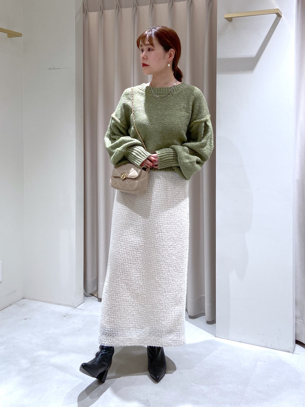グリーン系のニット/セーター、ホワイト系のスカート、ベージュ系のショルダーバッグを着用したレディースの秋コーディネートの3枚目の写真