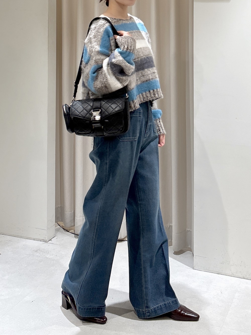 グレー系のニット/セーター、ブラック系のショルダーバッグ、ブルー系のデニムパンツを着用したレディースの秋コーディネートの2枚目の写真