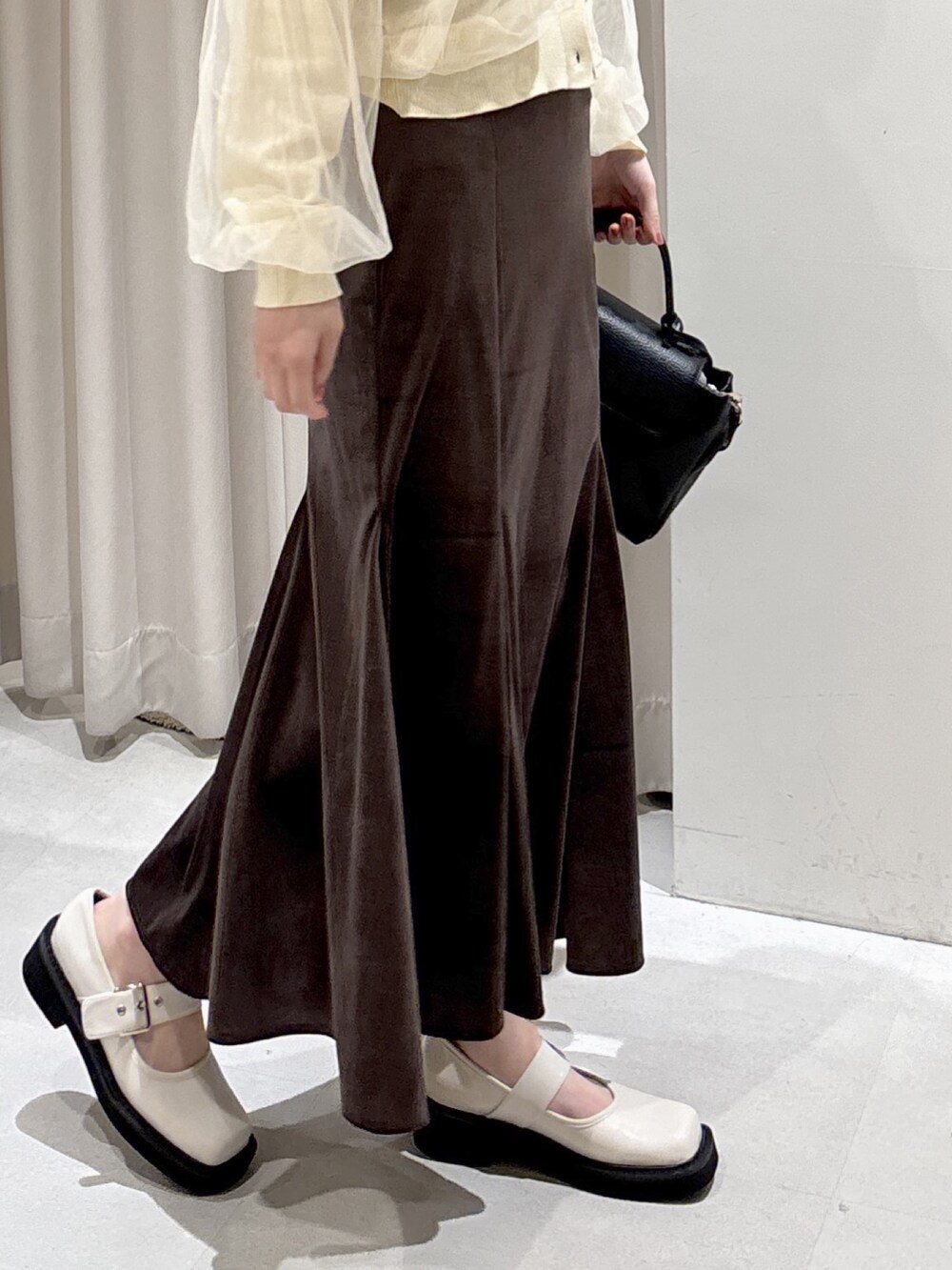 イエロー系のニット/セーター、ブラウン系のスカート、ブラック系のショルダーバッグを着用したレディースの冬コーディネートの3枚目の写真