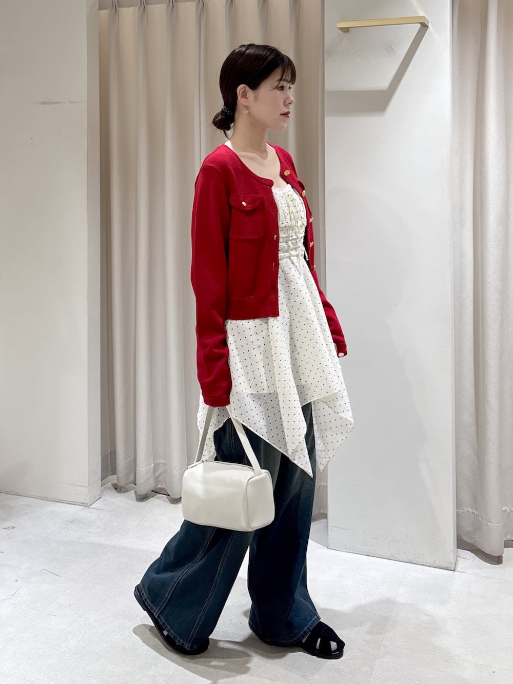 レッド系のニット/セーター、ホワイト系のワンピース、ブルー系のデニムパンツを着用したレディースの春コーディネートの2枚目の写真