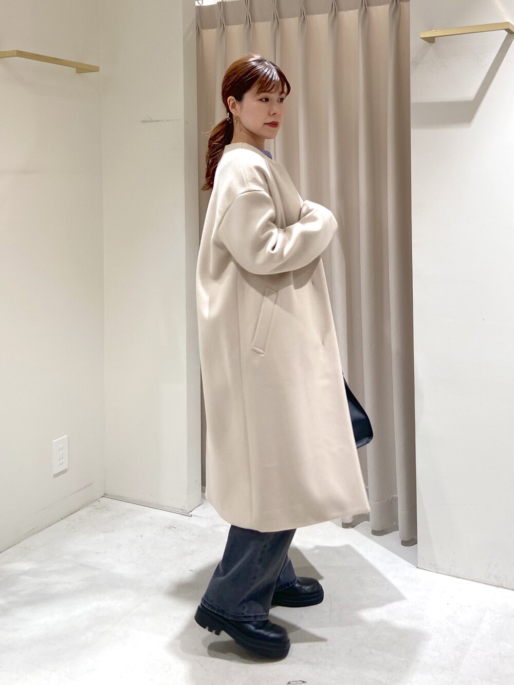 ベージュ系のノーカラーコート、ブルー系のニット/セーター、ブラック系のショルダーバッグを着用したレディースの冬コーディネートの2枚目の写真