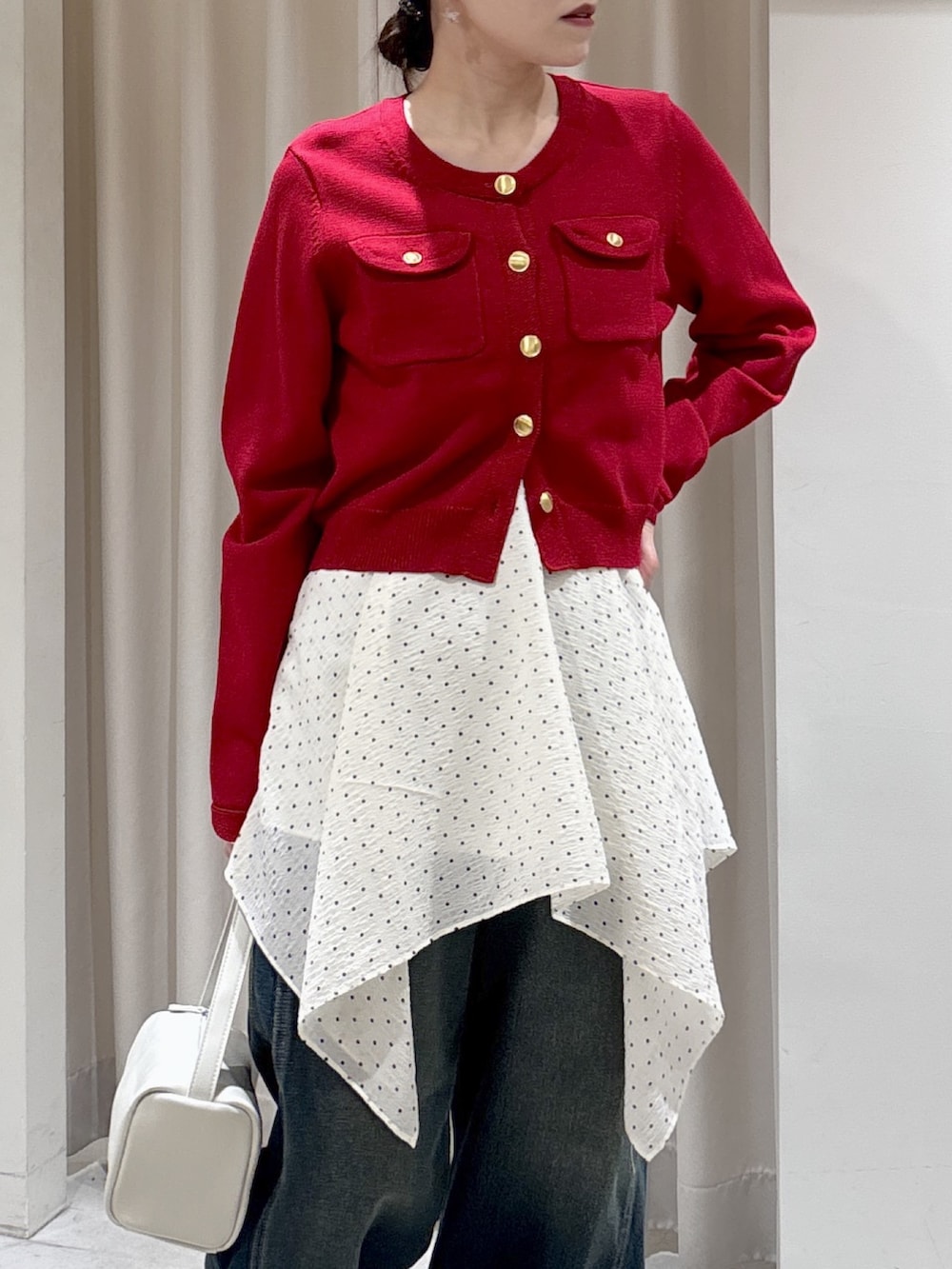 レッド系のニット/セーター、ホワイト系のワンピース、ブルー系のデニムパンツを着用したレディースの春コーディネートの4枚目の写真