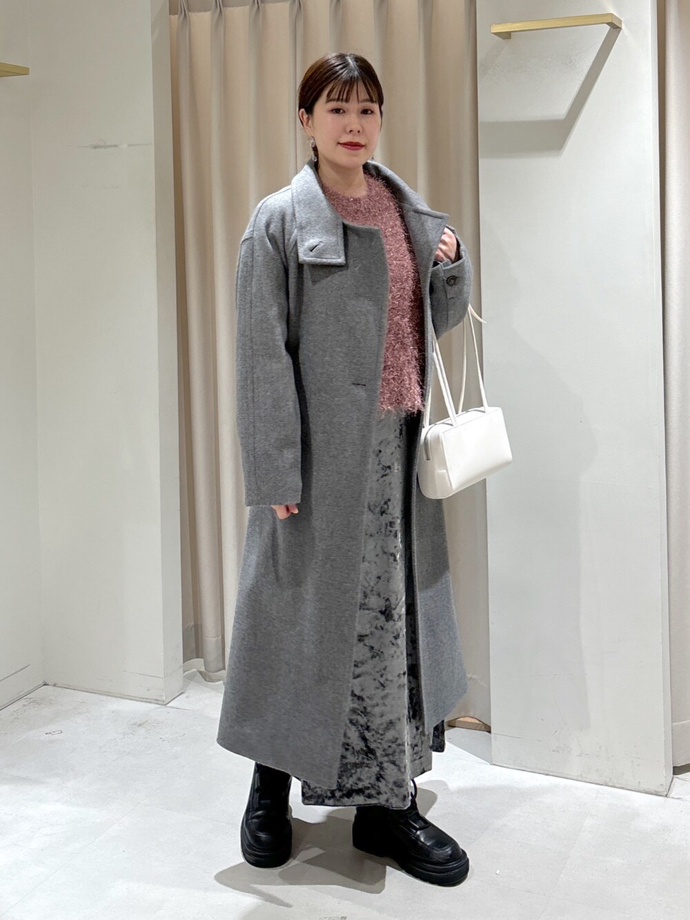 グレー系のステンカラーコート、ホワイト系のショルダーバッグ、ブラック系のブーツを着用したレディースの冬コーディネートの3枚目の写真