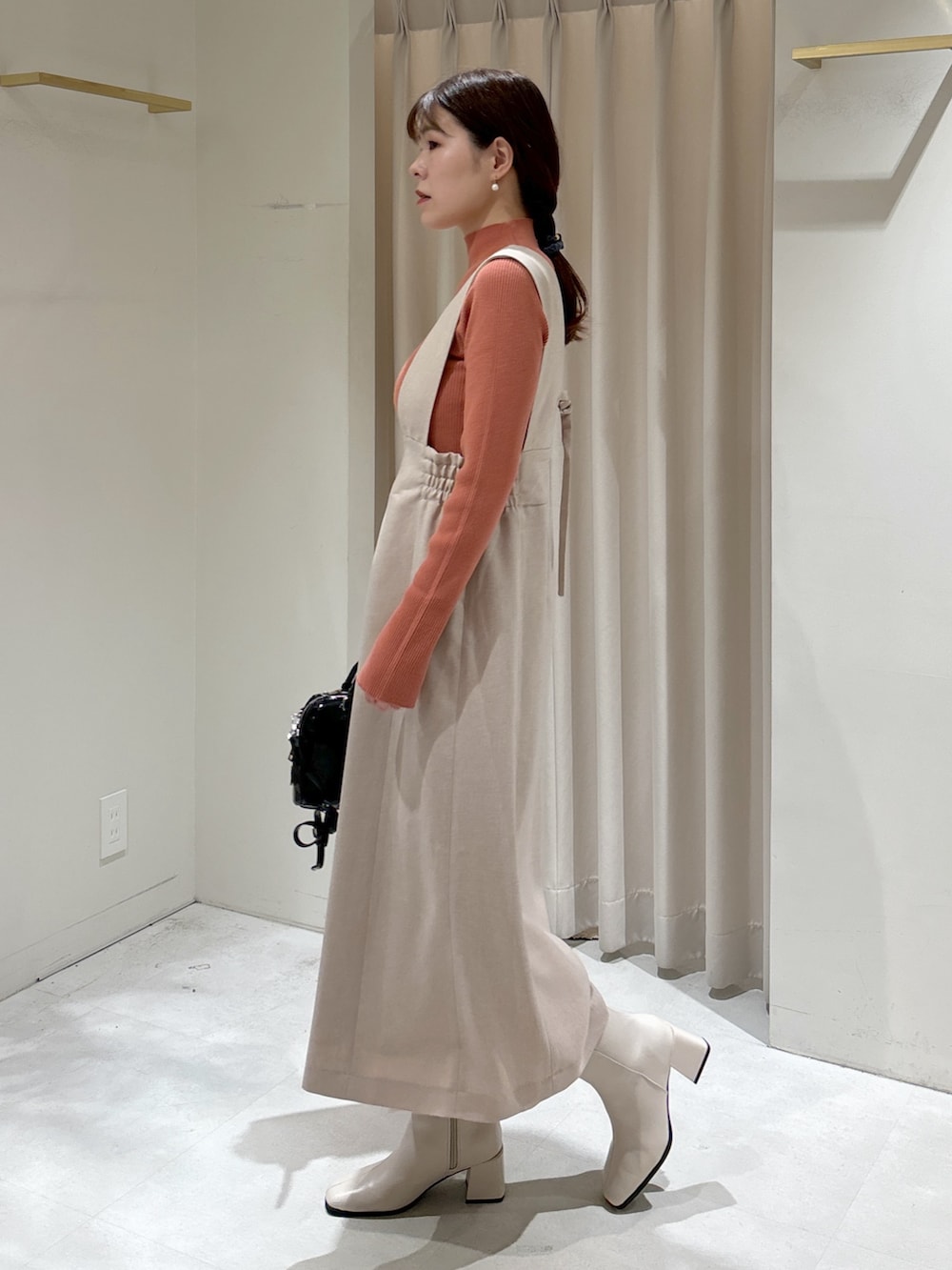 ピンク系のニット/セーター、ベージュ系のジャンパースカート、ブラック系のショルダーバッグを着用したレディースの冬コーディネートの2枚目の写真