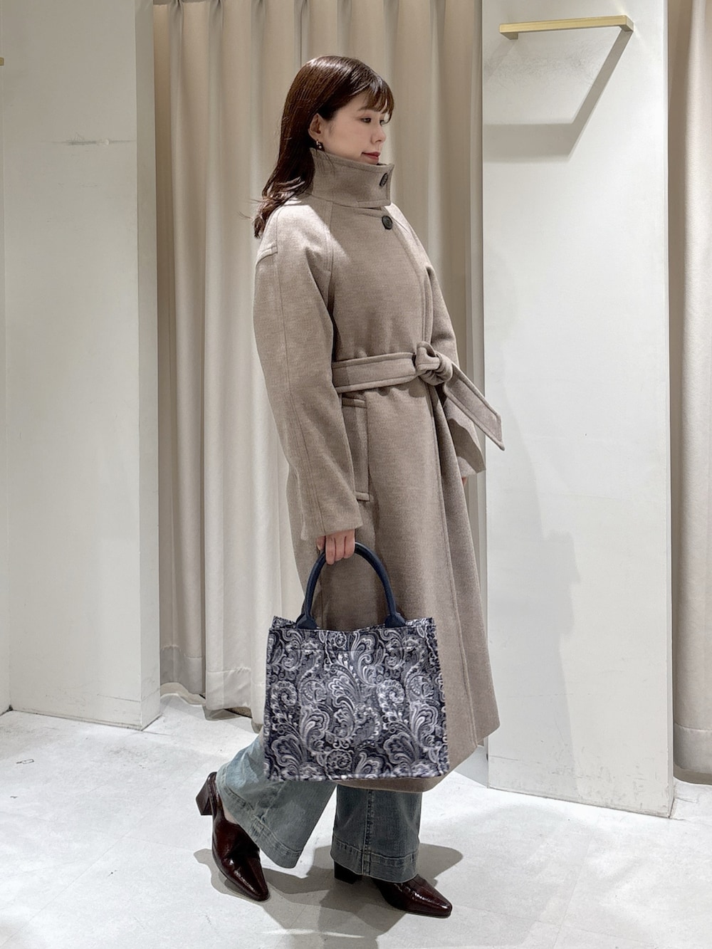 ブラウン系のステンカラーコート、ブルー系のトートバッグ、ブルー系のデニムパンツを着用したレディースの秋コーディネートの5枚目の写真