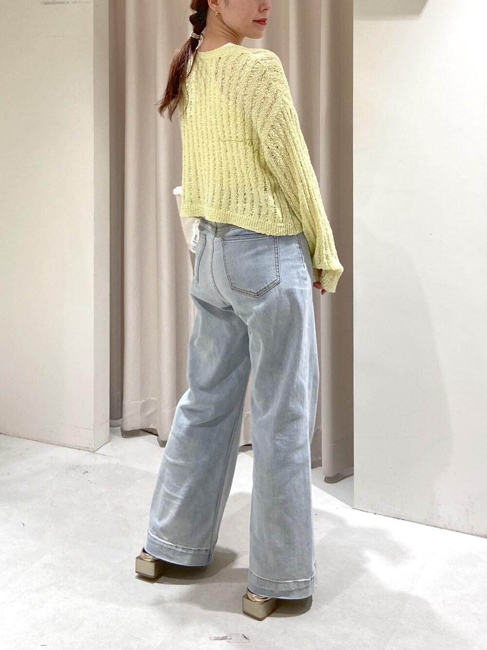 イエロー系のニット/セーター、シルバー系のトートバッグ、ブルー系のデニムパンツを着用したレディースの春コーディネートの2枚目の写真