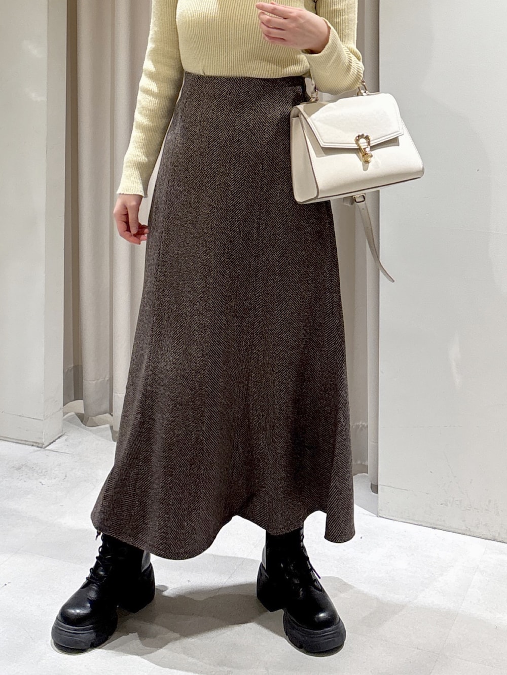 イエロー系のニット/セーター、ブラウン系のスカート、ブラック系のブーツを着用したレディースの秋コーディネートの3枚目の写真