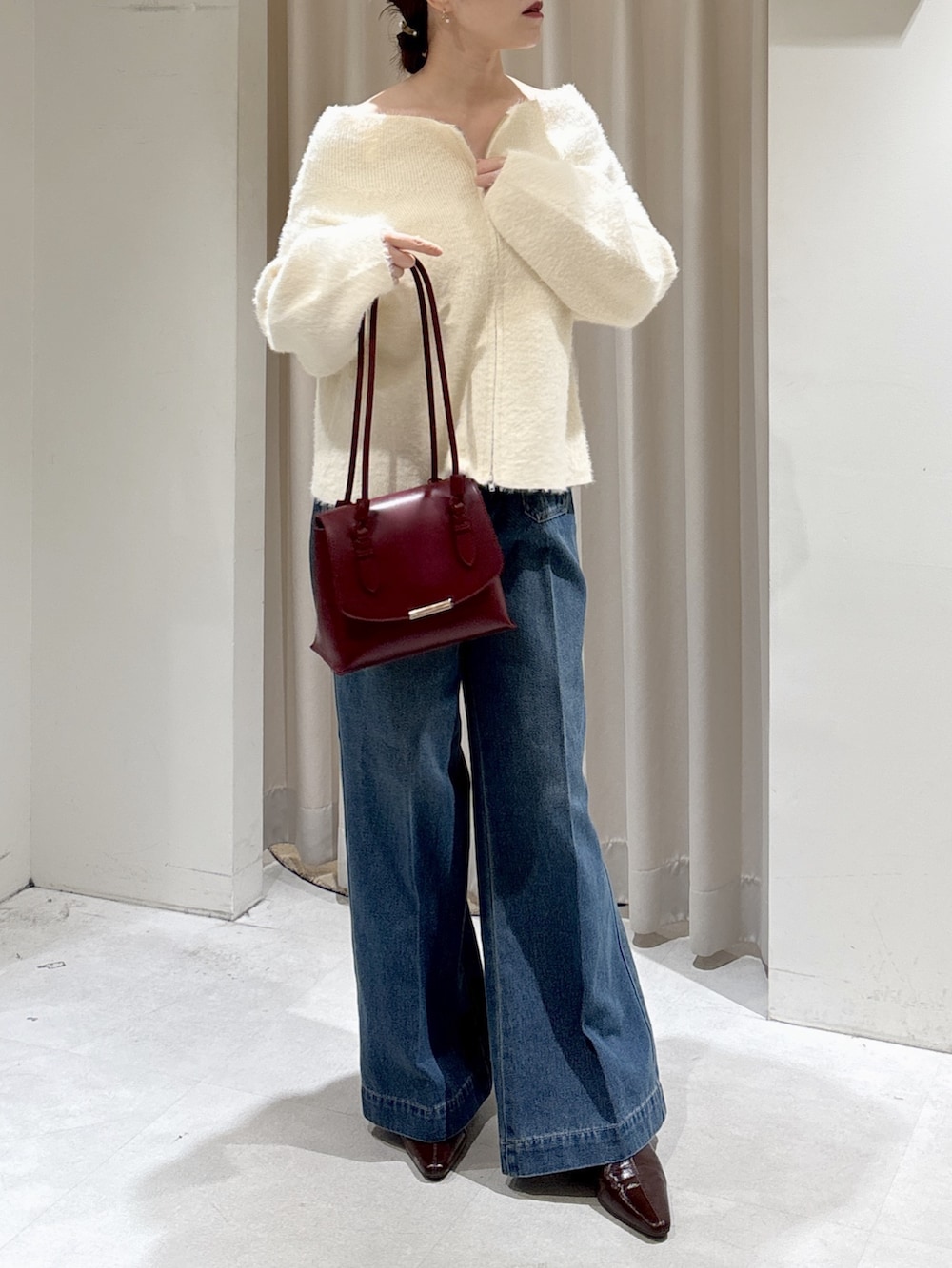 ホワイト系のニット/セーター、レッド系のトートバッグ、ブルー系のデニムパンツを着用したレディースの秋コーディネートの2枚目の写真